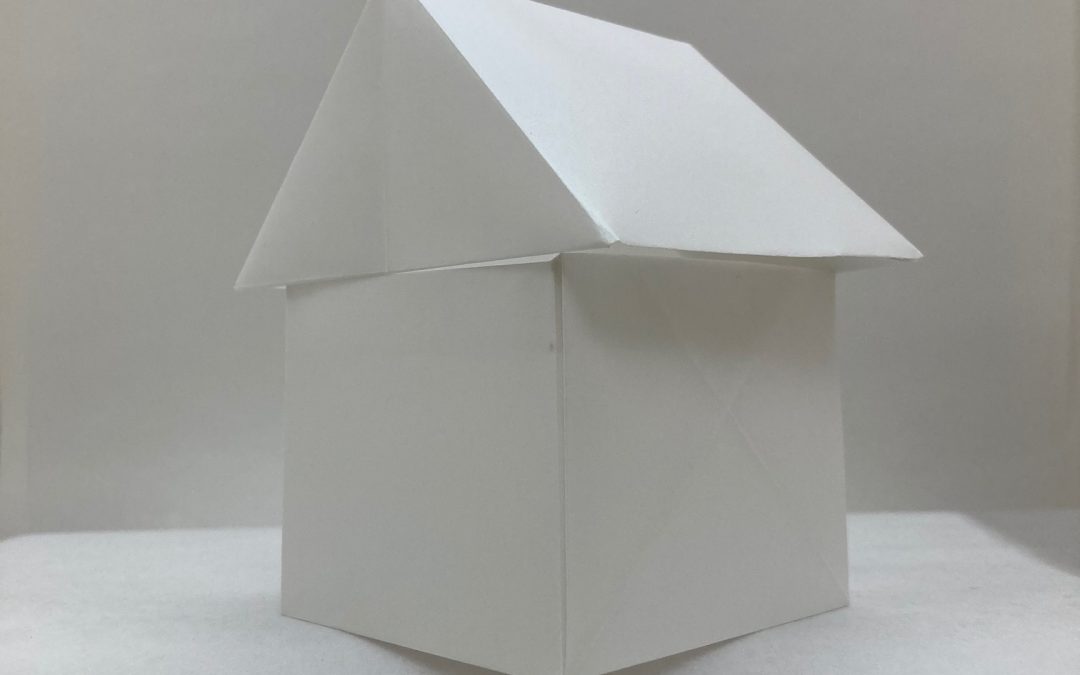A fragile, paper house sits precariously at the edge of a smooth white cliff.